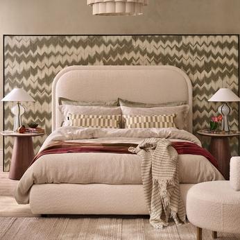 A cream coloured bed in a green and cream patterned room