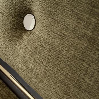 Close up of an olive green chenille sofa with gold button detail and wooden trim
