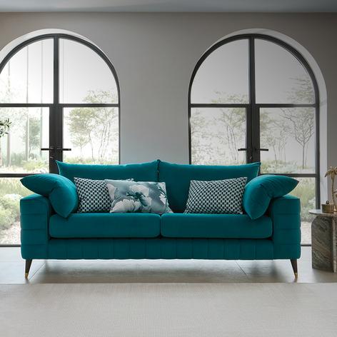 teal sofa on chrome feet with patterned scatters in a room with floor to ceilin glass doors behind