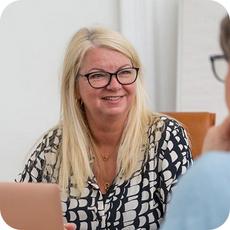 image a person with long blonde hair and glasses talking to someone just out of frame