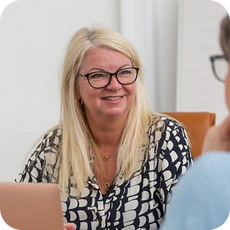 image a person with long blonde hair and glasses talking to someone just out of frame