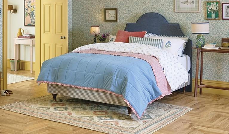 Navy bed with wooden detail against a striped wallpaper wall