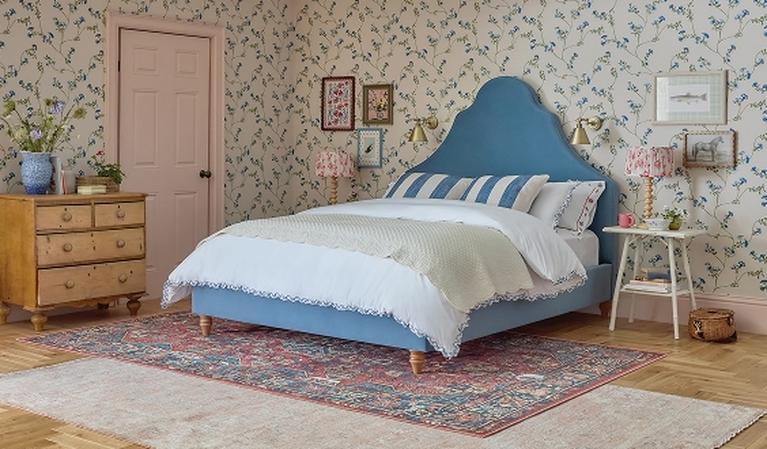 Blue pattered bed with wooden detail against a pink wall