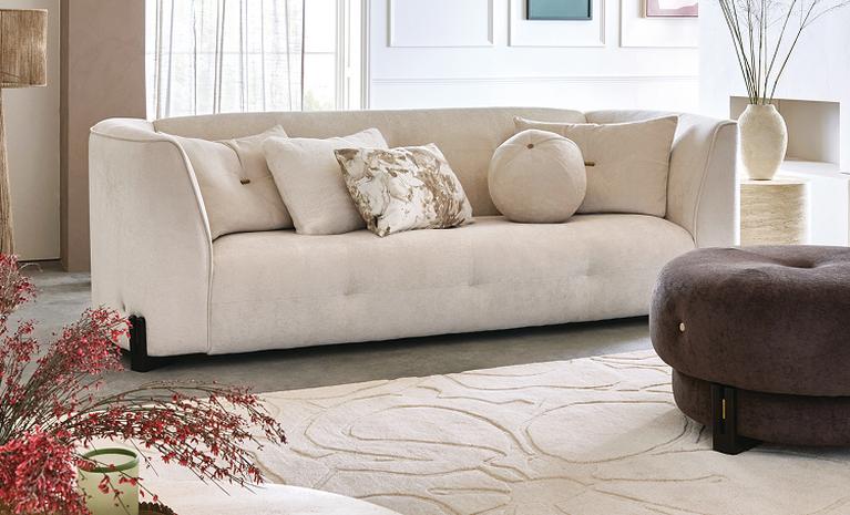 cream curved sofa with brown footstool in a neutral roomset