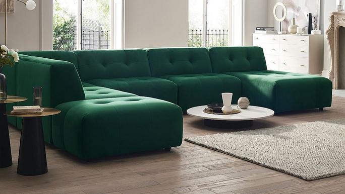 Green buttoned u shaped corner sofas with a white coffee table on a wooden floor and fluffy rug 