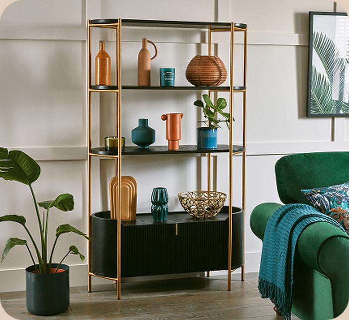 Black and gold bookshelf next to a plant and green sofa