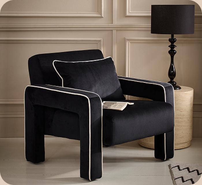 Black velvet accent chair next to a cream side table with a black lamp