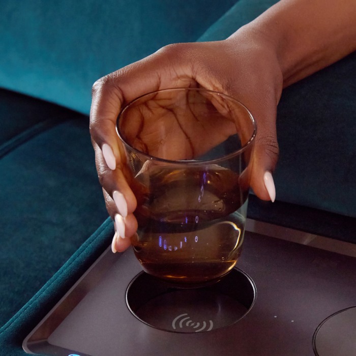 A hand reaching for a glass resting in a cup holder and wireless charger