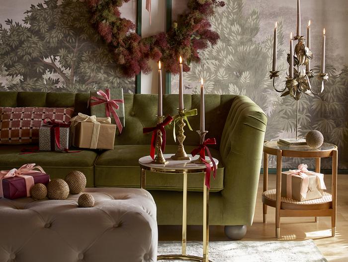 Dark green chesterfield sofa with christmas decorations of candles, presents and a wreath with red and green 