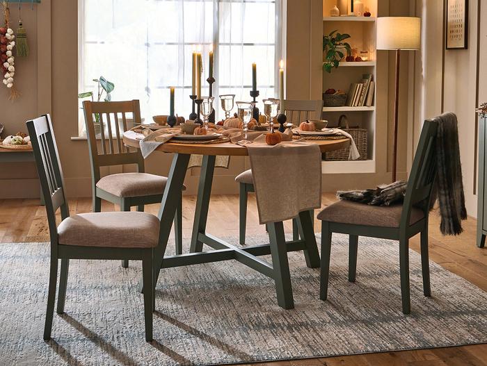 Sage green and wood round dining table set with a halloween themed decor with pumpkins and candles 