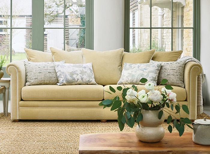A yellow sofa on a beige rug with a vase of flowers