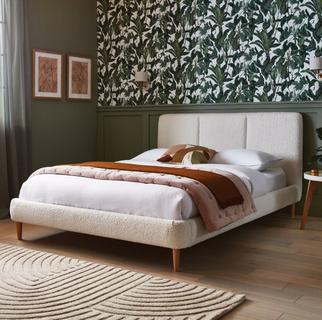 A cozy bedroom featuring a boucle white bed, adorned with a brown throw, against a floral wallpaper backdrop