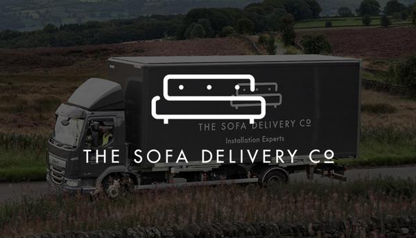 Grey truck with sofa delivery company on and a man in a high vis jacket greeting an older mn