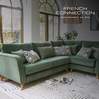 Sage green corner sofas on wooden feet next to two large oval windows and on top of a monochrome patterend rug