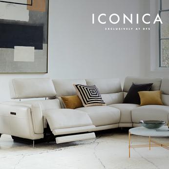White Leather recliner corner sofa in a bright clinical living space with yellow and monochrome scatters next to a glass top coffee table 