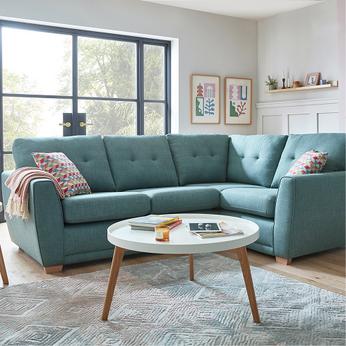 Pale blue corner sofa with buttoned cushions in a bright living room with a white round coffee table with wooden legs