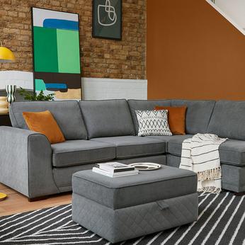 Dark Grey corner sofa in a rustic living room with a orange and brick wall and monochrome and orange scatters