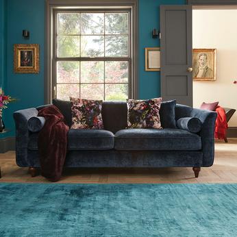 Navy blue sofa with floral purple scatter cushions next to a blue wall and a fluffy blue rug