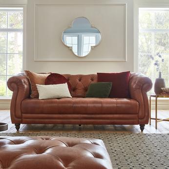 Brown leather chesterfield sofa with green and red scatter cushions with a matching buttoned brown leather footstool