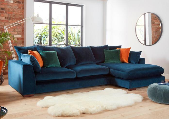 blue velvet corner sofa with orange and green scartters