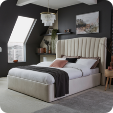 cream quilted divan bed next to a black wall and light bedding
