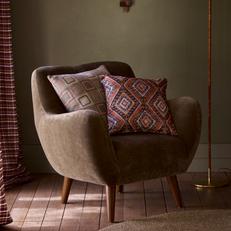 Brown winged accent chair with walnut angled legs with pink patterned scatter cushion next to an olvie green wall