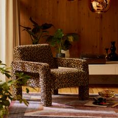 Wylde leopard print accent chair in a dark wooden room next to an orange patterned rug