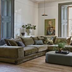 Olive green corner sofa in a moody dark room with natural lighting and a geometric footstool