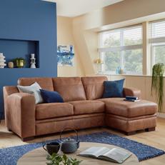 Brown leather corner sofa with blue and monochrome scatter cushions next to a blue rug