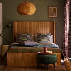 wooden pannelled bed next to an olive green wall with patterned scatter cushions