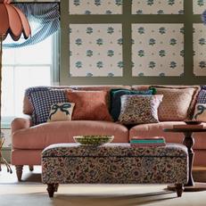 pink sofa next to a green panelled wall and a floral footstool with floral scatter cushions