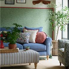 blue fabric sofa against a green floral wall and a stripy footstool