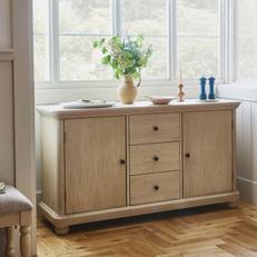 light wood sideboard with three drawers and two cupboards next to a large window