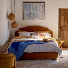 Orange bed finished with white bedding and a blue throw with a rattan hanging light and blue and white canvas