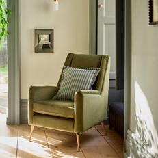 Olive green accent chair with gold metal legs next to green curtains