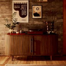 Dark wood panelled sideboard with black metal handles next to a dark brick wall with artwork
