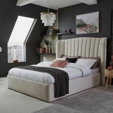 Cream velvet bed next to a black wall with monochrome decor