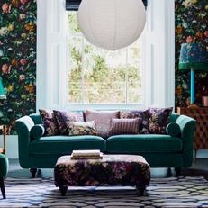 Teal coloured sofa with floral scatter cushions and floral wallpaper