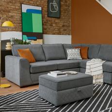 Grey corner sofa with oranger and monochrome scatters next to an orange wall