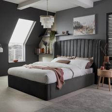 Dark grey fluted bed with white bedding and a pink throw next to a dark grey wall