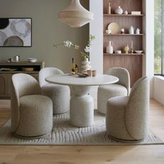 Cream round dining table with four light grey round boucle dining chairs next to walnut shelf
