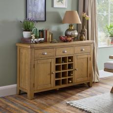 Oak sideboard with wine rack next to a sage green wall filled with lamps and accessories