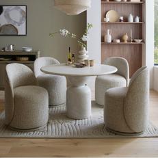 White round marble dining table with light grey fabric chairs next to a walnut bookshelf