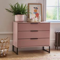 pink 3 drawer chest of drawers with black metal feet and handles topped with a plant a colourful picture