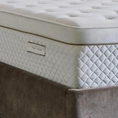 A quilted mattress with gold pipiing on a brown velvet bed