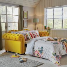Yellow chesterfield sofa bed with floral beddding and patterned scatter cushions