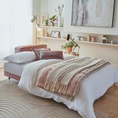 Pink 3 seater fold out sofa bed with a pale pink throw in a bright and airy room