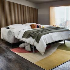 Grey fold out sofa bed with grey throw next to a wooden panelled wall