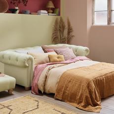 Cream leather chesterfield sofa with a pink and brown throw and cushions next to a yellow wall
