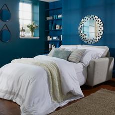 White leather sofa bed with white bedding next to a dark blue wall with mirror